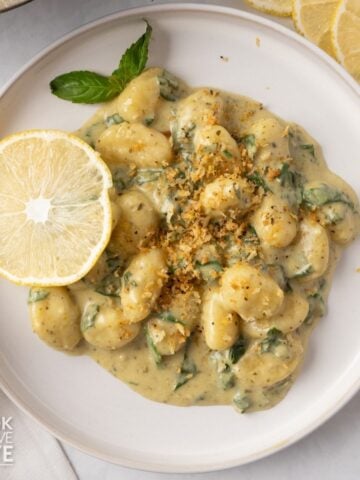 A plate with creamy pesto gnocchi and a lemon on the side.