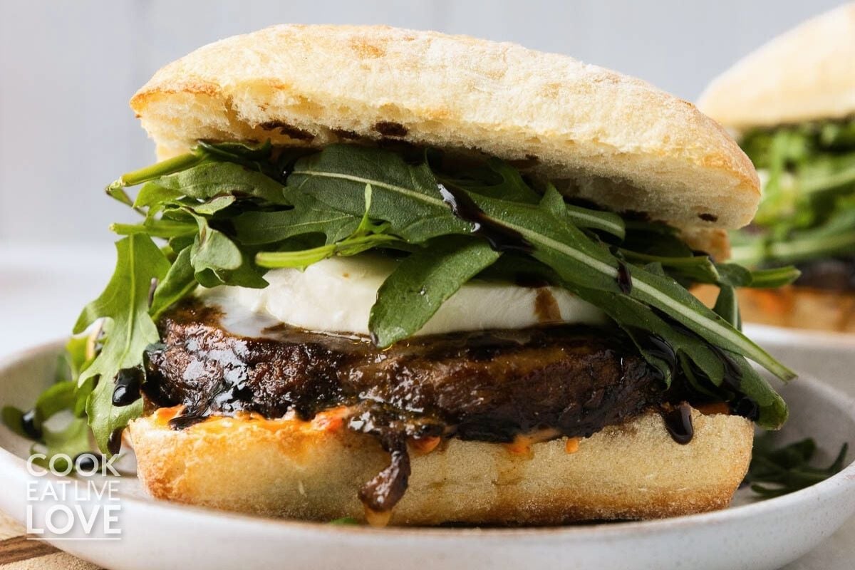 A portobello mushroom sandwich on a ciabatta roll with s mushroom, mozzarella, arugula, and balsamic glaze.