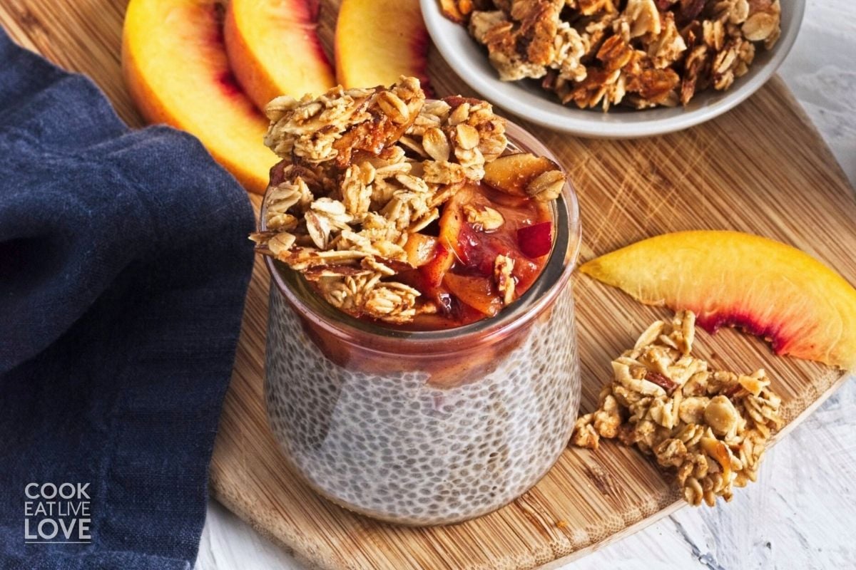 Peach chia pudding jar on a wooden cutting board with sliced fresh peaches and granola. 