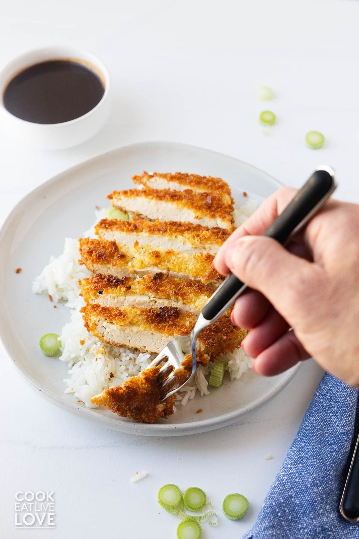 A fork stabbing a slice of tofu katsu on a white plate. 