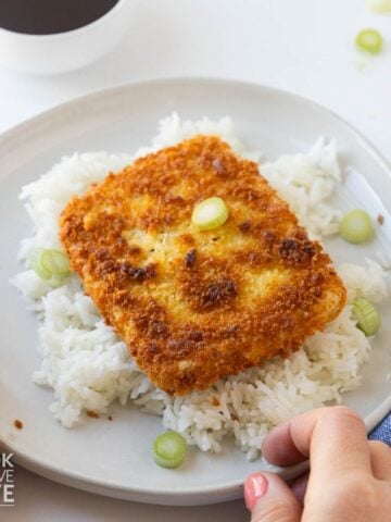 A white plate of rice and tofu katsu garnished with green onions.