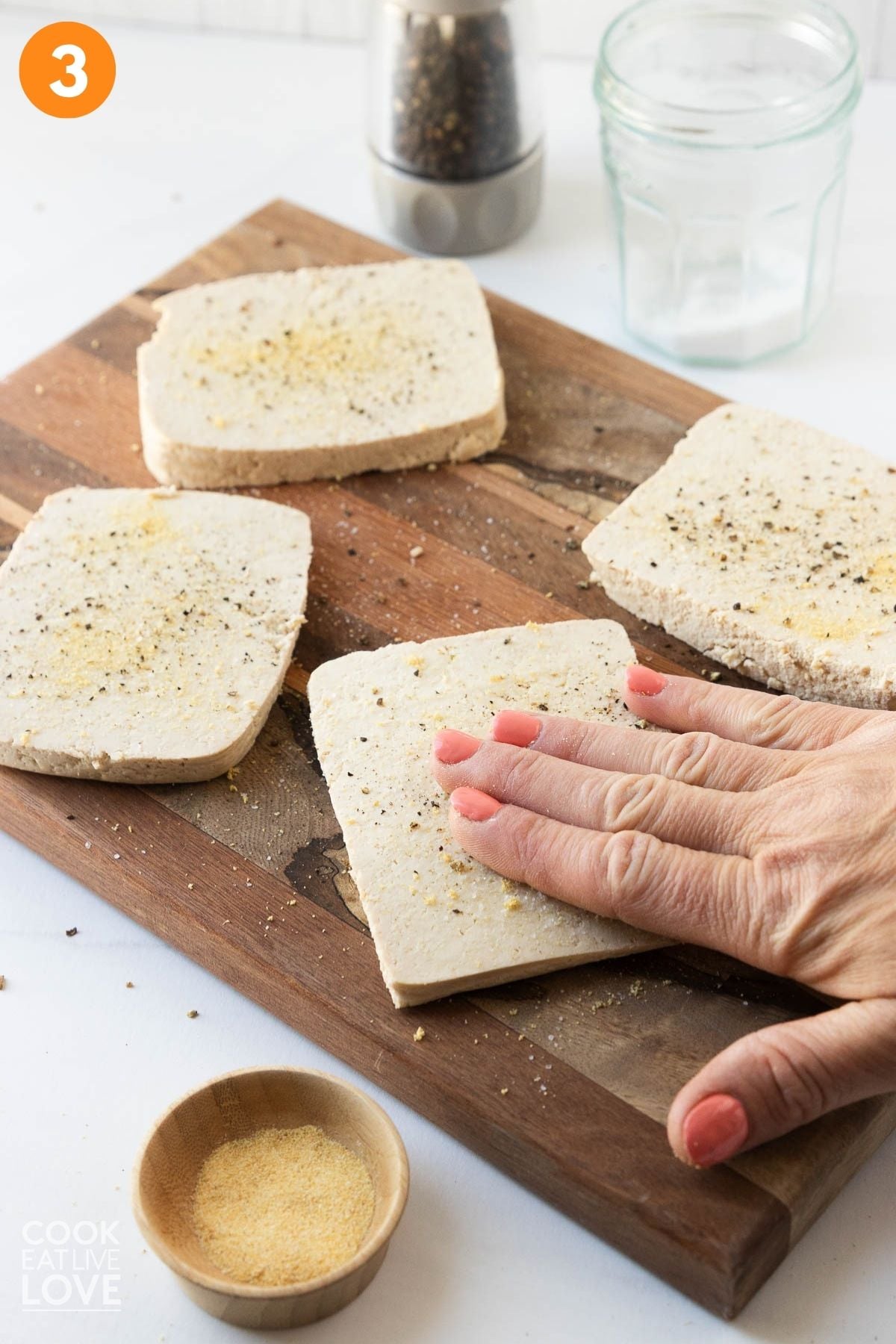 A hand pressing the seasonings on the tofu.