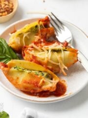 Three vegan stuffed shells served up on a white plate and garnished with basil leaves.