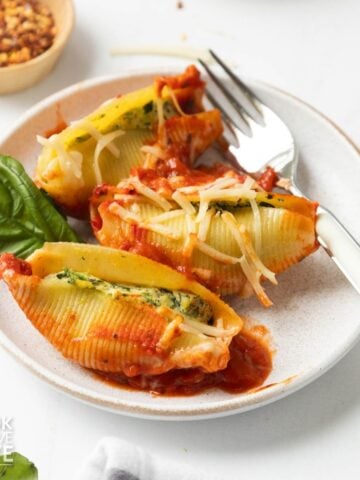 Three vegan stuffed shells served up on a white plate and garnished with basil leaves.