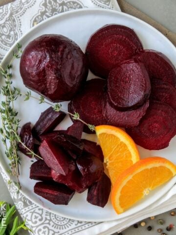 Oven roasted beets recipe serve on a white plate and garnished with orange slices and fresh herbs.