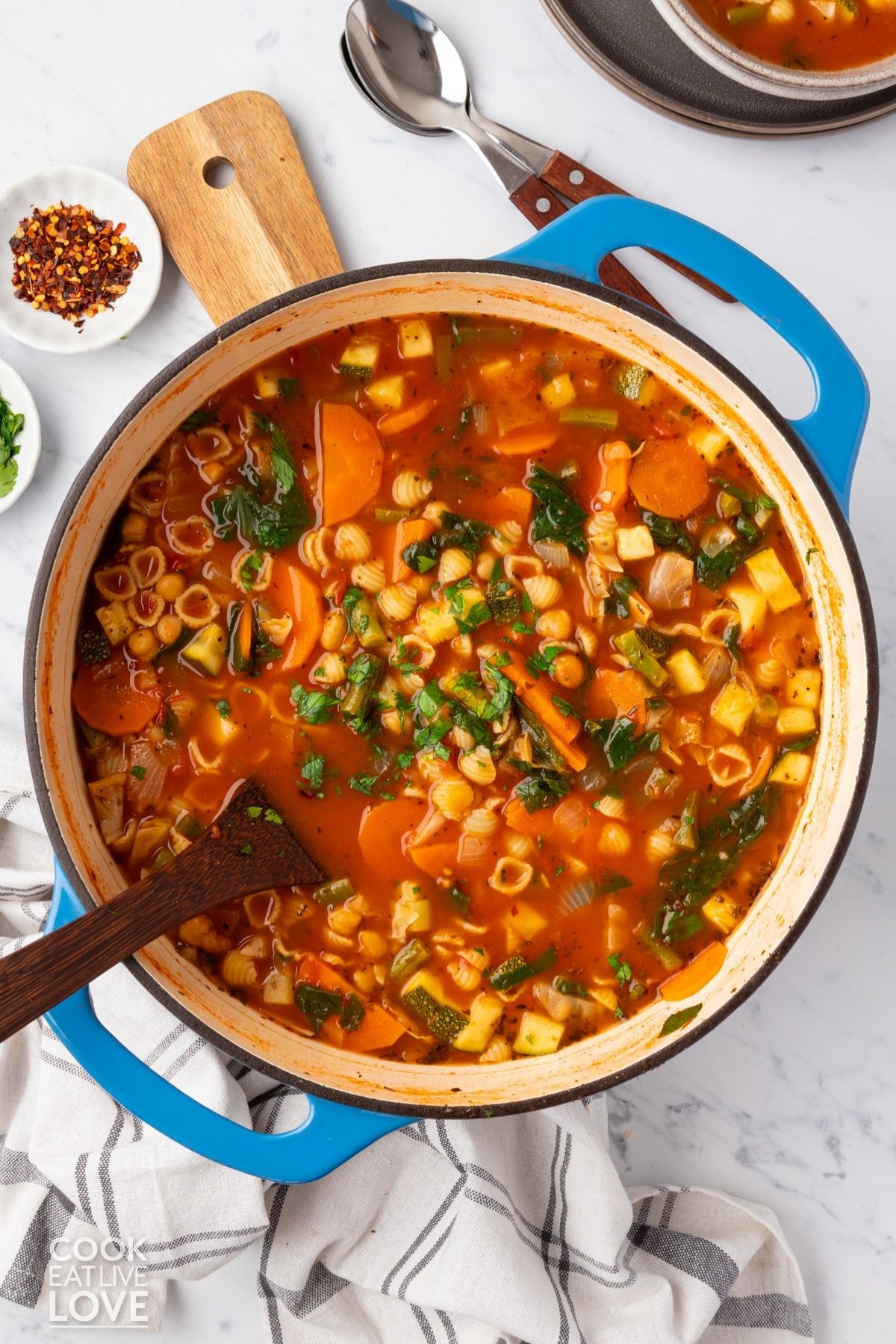 A pot of vegan minestrone soup with a wooden utensil resting in the bowl.