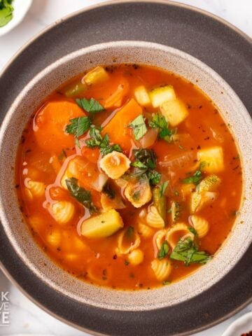 A bowl of vegan minestrone soup on a brown plate.