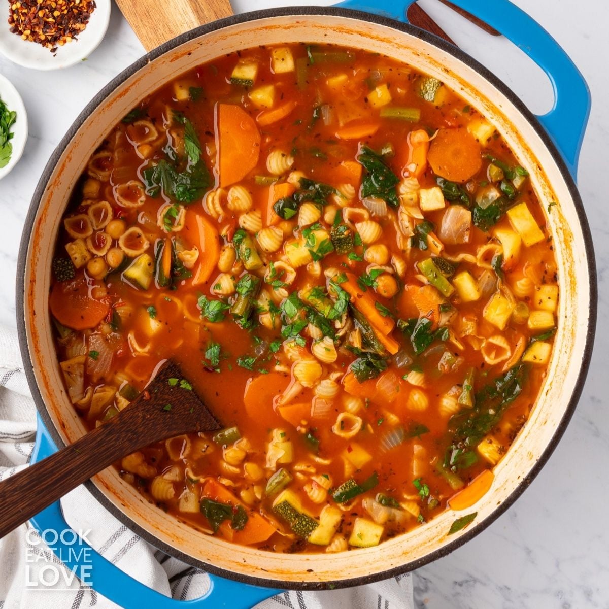 A pot of vegan minestrone soup with a wooden spoon resting on the side.