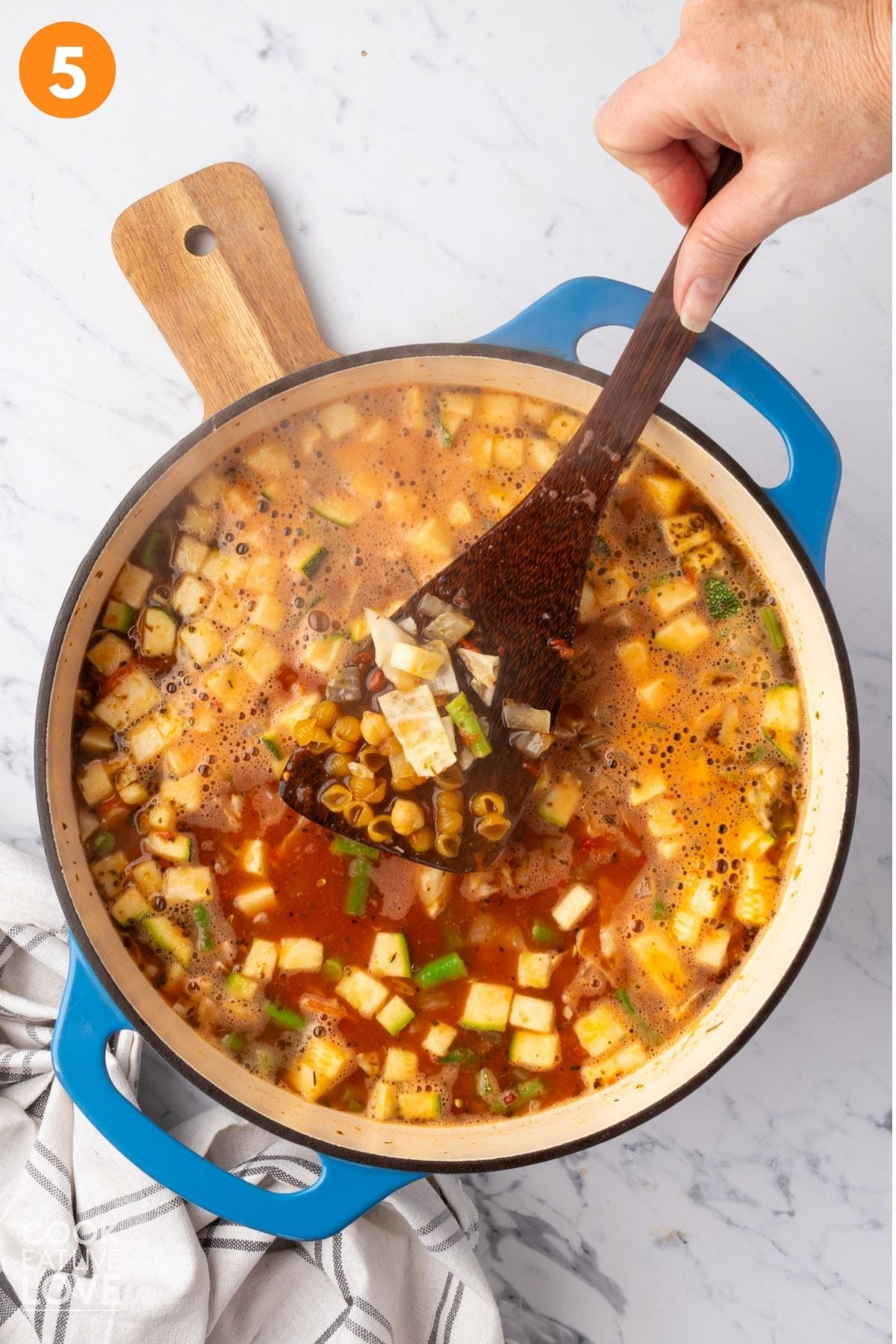 A spoon lifting up the pasta added to pot of minestrone soup. 