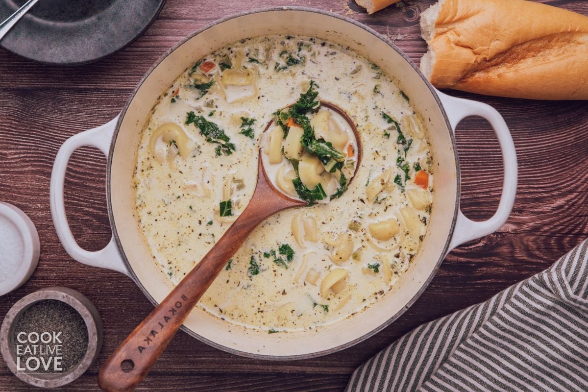 A pot of vegetarian tortellini soup with a spoon resting in the pot.