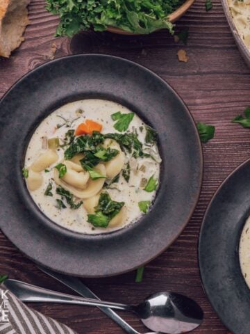 Bowls of cheese tortellini soup with some bread and the pot to the side.