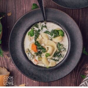 A bowl of cheese tortellini soup with a spoon resting in the bowl.
